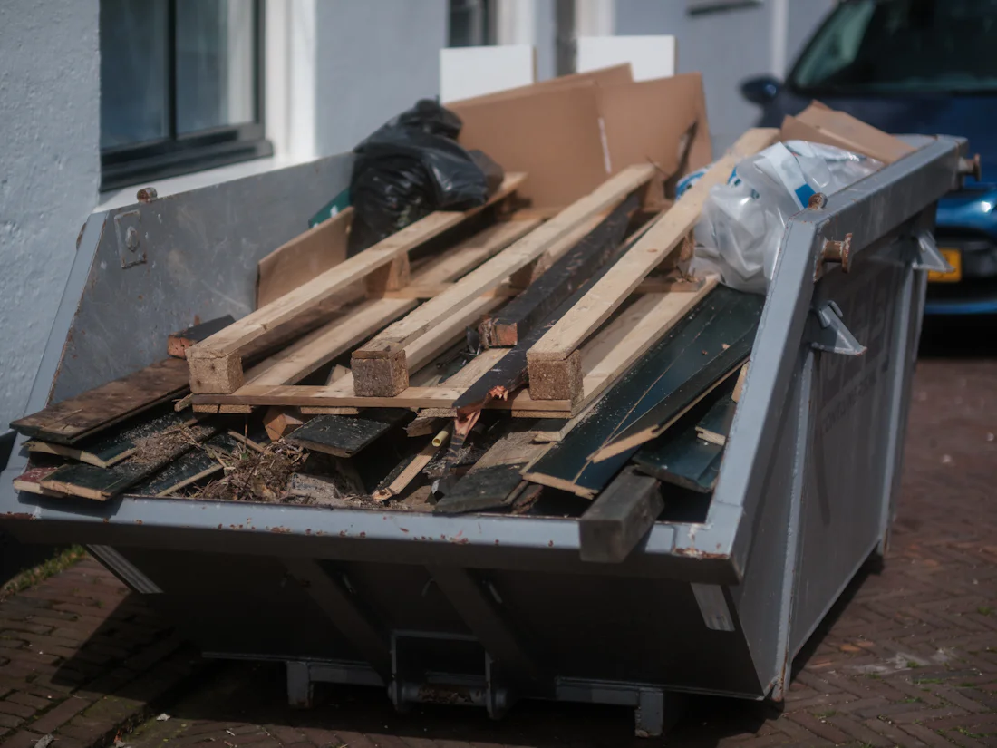Container vor einem Haus, gefüllt mit Holzpaletten, Brettern und Kartons