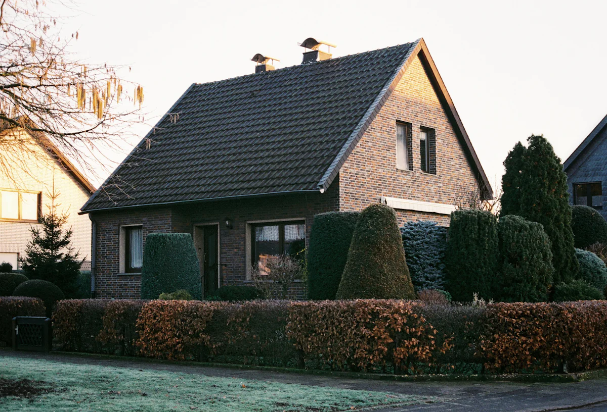 Gepflegtes Klinkerhaus mit sauber geschnittener Hecke und Formgehölzen im Vorgarten