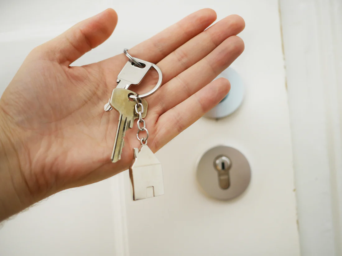 Hand hält einen Schlüsselbund mit Haus-Anhänger vor einer Haustür